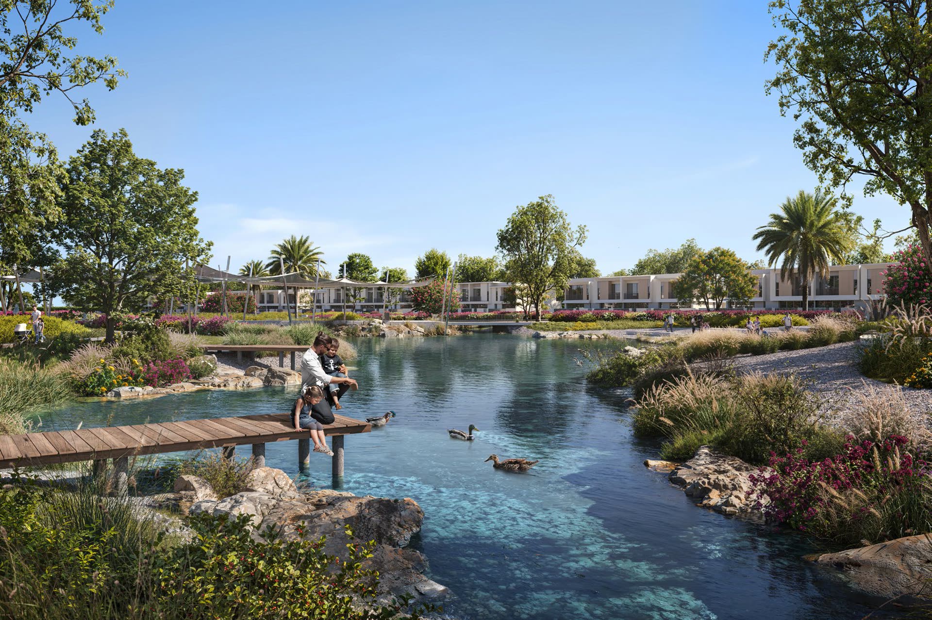 Families beside the meandering river at The Valley, with townhouses along the far bank